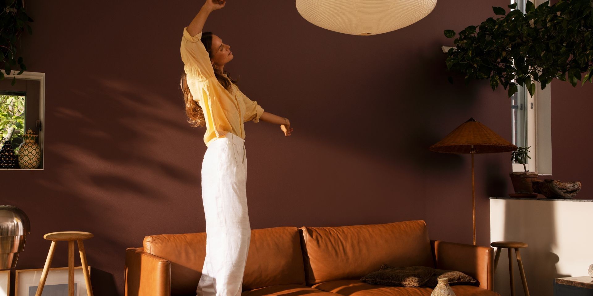 kobieta tańcząca w przytulnym salonie ze ścianą w kolorze ciepłego brązu i kanapą