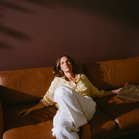 kobieta relaksująca się na brązowej skórzanej kanapie na tle ściany w kolorze ciepłego brązu