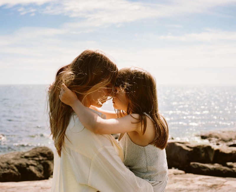  matka i córka przytulające się na kamienistej plaży w słoneczny dzień