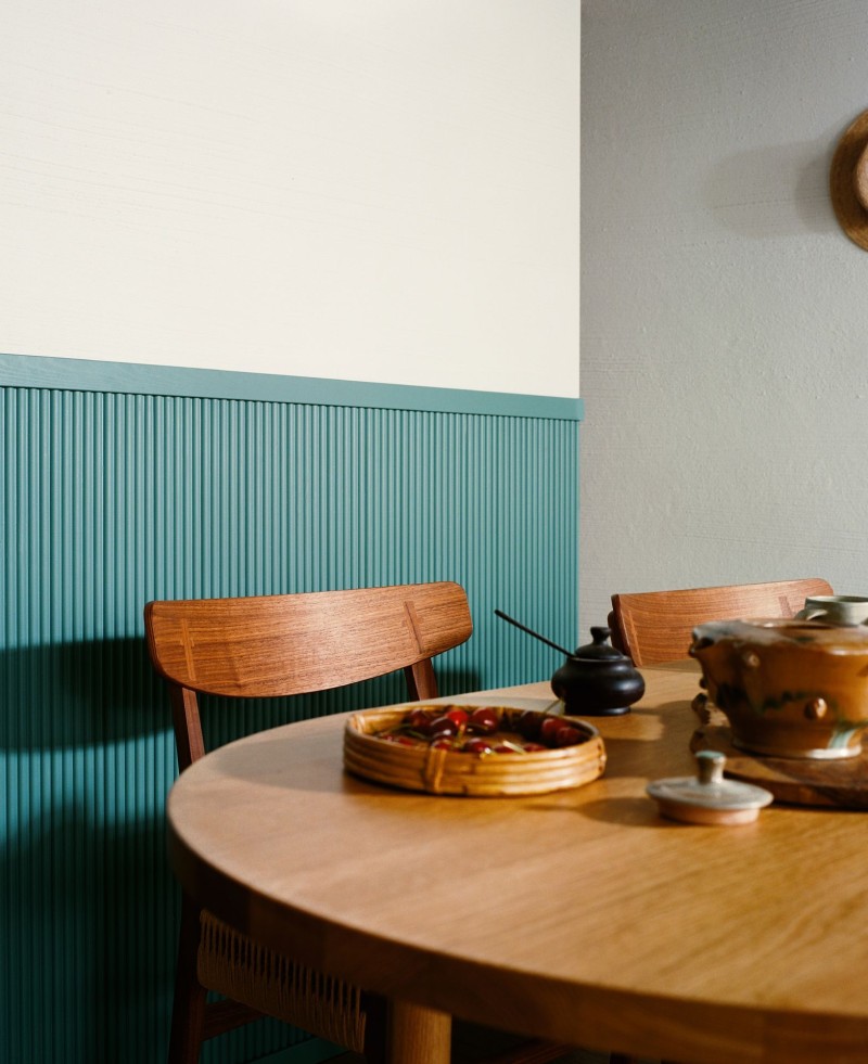 stół w kolorze naturalnego drewna i zielono-niebieska boazeria w tle